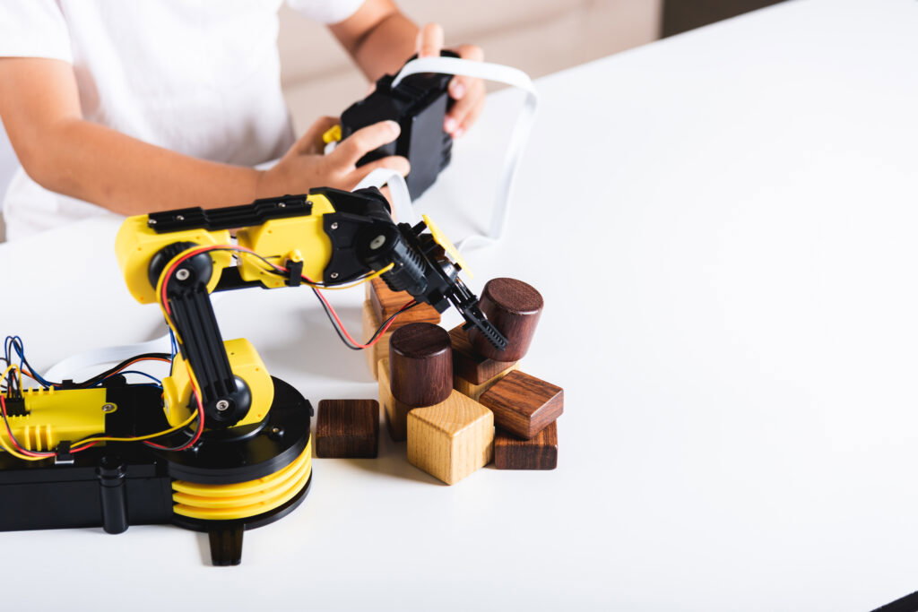 Happy Asian little kid boy using remote control playing robotic machine arm for pick up wood block