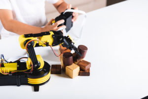 Happy Asian little kid boy using remote control playing robotic machine arm for pick up wood block